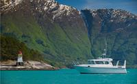 Pilagutt ligg til kai i Hardangerfjorden, omgitt av majestetiske fjell og turkist vatn. Den ultimate fjordopplevinga.