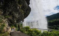 Nærbilde av besøkende som går under Steinsdalsfossen på en tilrettelagt sti, med vannet som faller kraftig i bakgrunnen og den norske naturen i full visning.