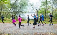 Group of people running in a race surrounded by autumn leaves and trees.