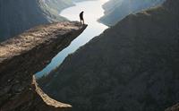 En person står alene på Trolltunga med utsikt over fjorden på en klar dag.