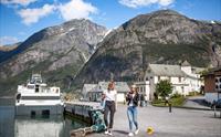 To kvinner går på kaia i Eidfjord med cruisebåten Fjorddrott fortøydd bak og bratte fjell i bakgrunnen.