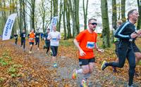 Group of people running in a race surrounded by autumn leaves and trees.