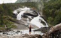 Kvinne ved elvekanten nedanfor Tveitafossen – den første fossen på fotturen gjennom Husedalen.