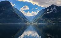 Fjord med spegling av fjell og himmel i stille vatn mellom høge fjell.
