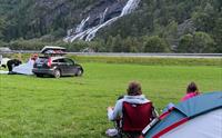 Gjester slappar av ved telt på Hildal Camping med fossen som bakteppe.