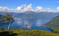 Utsikt frå Dronningstien over den blå fjorden og fjellene under ein klar himmel.
