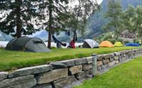 Telt på graset ved vatnet på Trolltunga Camping, omgitt av fjell og natur.
