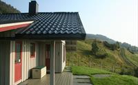 Tradisjonell norsk hytte med overbygd terrasse, raude dører og utsikt mot grøne åsar i Hardanger.