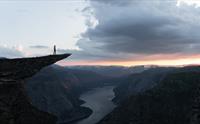 Person på Trolltunga ved solnedgang med utsikt over Ringedalsvatnet – høgdepunkt på Trolltunga Via Ferrata Sky Ladder.