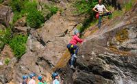 Deltakar i rosa jakke tek første steg opp bergveggen ved via ferrata-starten på Valhall i Odda, medan gruppa ventar på plattformen nedanfor.
