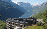 Hordatun Hotel sett frå sommarlandskap, med utsikt mot Røldalsvatnet og dei snødekte fjelltoppane i bakgrunnen.