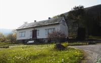 Hvitt trehus i Nestunet med steintrapp og blomstrende eng foran.