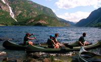 Familie på kanotur på fjorden med foss og grøne fjell i bakgrunnen.