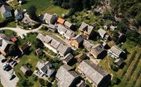 Dronefoto av Agatunet med historiske trehus tett samla, omgitt av grønt landskap og frukthager.