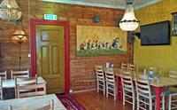 Inne i pannekakerestauranten. Bord og stoler. Et morsomt maleri med en kvinne og barn som løper etter en rullende pannekake.