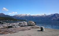 Utsikt over Hardangerfjorden med snødekte fjell og glatte svaberg ved vasskanten.