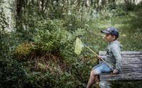 En liten gutt med hov sitter på en trebro i skogen.