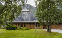 Eidfjord ny kirke sett fra utsiden, med fint grønt og et høyt fjell i bakgrunnen.