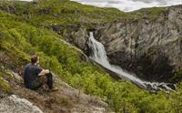 En mann sitter på bakken og stirrer mot Valurfossen nedenfor.