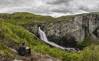 En mann sitter på bakken og ser på Valurfossen nedenfor.