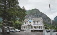 Viser Eidfjord Gjestgiveri fra utsiden. Det er et stort trehus, hvitt, med treskårne detaljer.