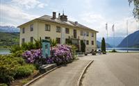 Haugesenteret ligg vakkert til ved fjorden i Hardanger, med fjell og blømande rododendron i bakgrunnen.