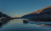 En båt med passasjerer i redningsvester kjører gjennom Sørfjorden ved solnedgang.