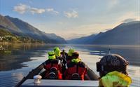 Passasjerer i en RIB-båt nyter en rolig tur på Sørfjorden med speilblankt vann og fjell i det fjerne.