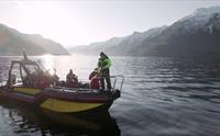 En gruppe fiskere forbereder seg på å fiske ombord på en båt på Sørfjorden med fjell og morgensol i bakgrunnen.