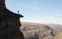 Person står på en massiv fjelltopp og ser utover fjellandskapet.