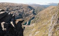 Person står på en massiv fjelltopp og ser utover fjellandskapet.