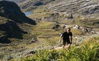 Person vandrer oppover i grønt fjellandskap.
