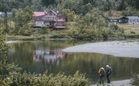 To turgåere står ved elvebredden og stirrer mot fjellstua over elva.