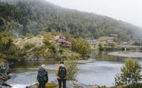To kvinnelige turgåere som står over elva fra fjellstua.