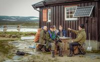 En gruppe menn sitter rundt et bord og snakker og smiler.