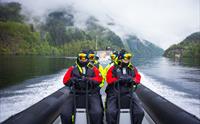 Ribbåt reiser gjennom eit grønt og frodig fjordlandskap med lavthengande skodde.
