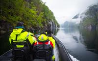 Ribbåt siglar roleg gjennom det spegelblanke vatnet i Fyksesund, med fossar og grøne åsar rundt.