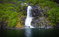 Ein kraftig foss omkransa av grøn vegetasjon langs Fyksesund i Hardanger.