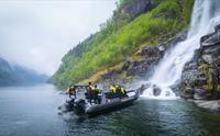Turistar i ribbåt beundrar ein foss som renn ned i Hardangerfjorden.