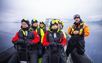 Ei gruppe glade turistar klare for eventyr på ein ribbåt på stille fjordvatn i Hardanger.