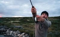 Et nærbilde av en mann som kaster ut snøret i et fjellvann.