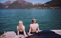 Utsikt bakfra av et par som sitter på bryggen og ser utover Sørfjorden i Hardanger.