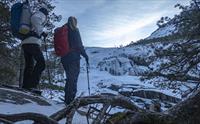 To vandrere ser på et frossent fossefall i et snødekt landskap i Husedalen.