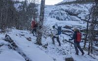 En gruppe vandrere navigerer seg oppover i et snødekt og steinete terreng.