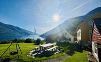 Solfylt uteområde ved Jaastad Gjestetun med sitjeplassar, grønt tun og utsikt over Hardangerfjorden og fjella.