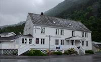 Fasade av Jondal Hotel på ein regnvêrsdag, med historisk arkitektur og fjell i bakgrunnen.