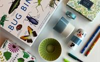 Eit utval varer frå museumsbutikken: spel, kortstokk, fargerike koppar, tusjar, blyantar og små gåveartiklar lagt ut på eit bord.