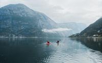 Et par padler kajakk på fjorden mot et stort fjell.