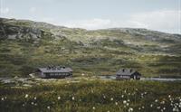 De to brune fjellstuene på Kjeldebu med fjell i bakgrunnen.