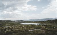 Et lite fjellvann under en skyet himmel.